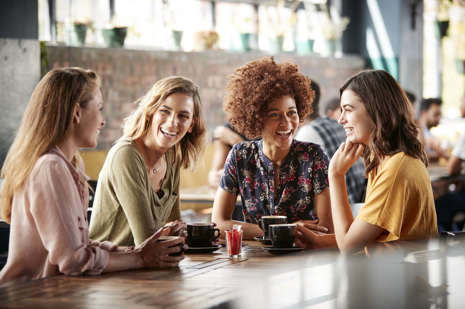 Four women talking and laughing over coffee at a café table.